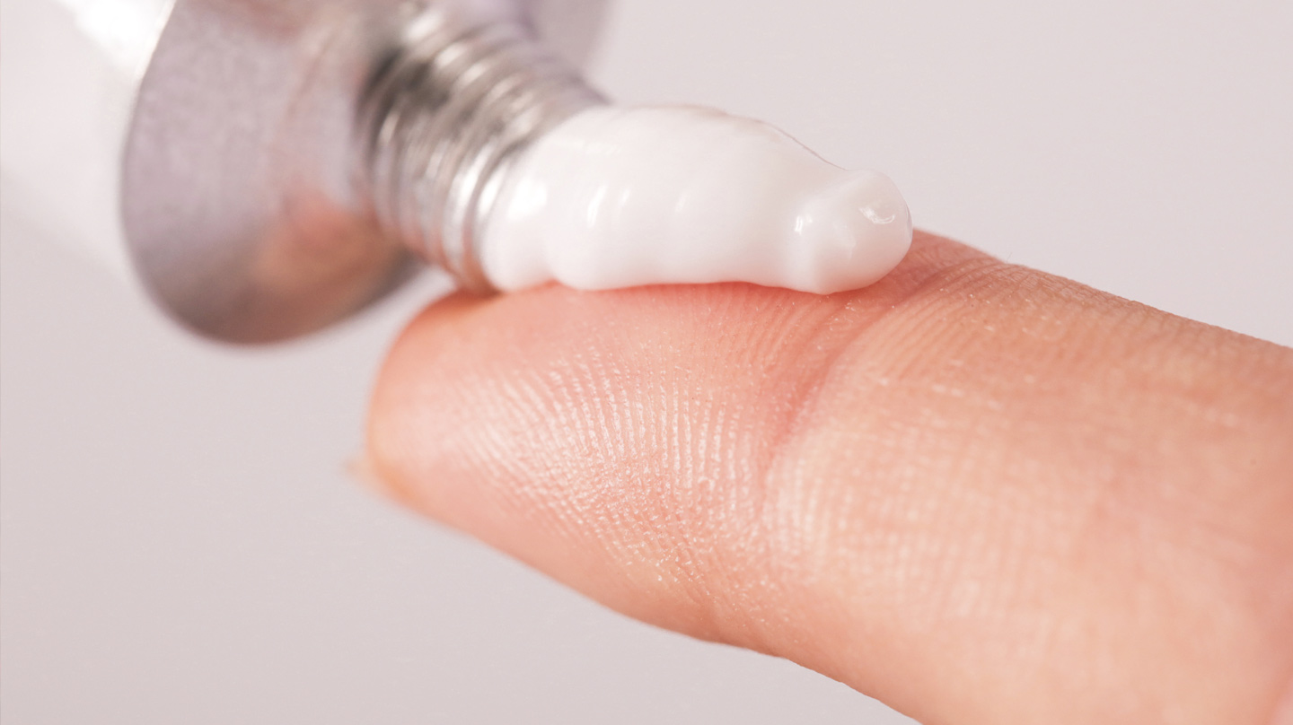 Kortisonsalbe: Ein kurzer weißer Salbenstrang wird aus einer Tube auf die Fingerspitze gedrückt.
