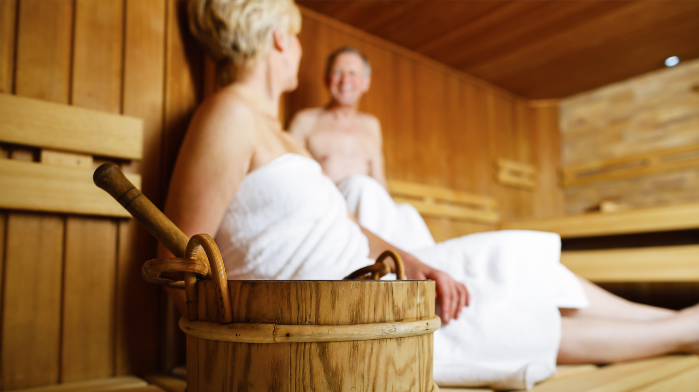 Richtig saunieren: Älteres Ehepaar in weiße Handtücher gehüllt in der Sauna.